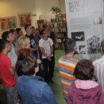 Grupa osób ogląda wystawę posterową w bibliotece.