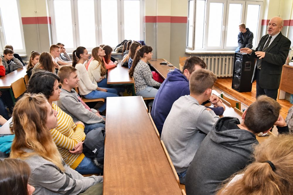 Prelegent zwrócony do grupy młodzieży siedzącej przy stolikach w klasie.