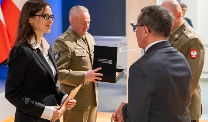 Dwóch oficerów i dwoje cywilów w trakcie wręczania nagrody.