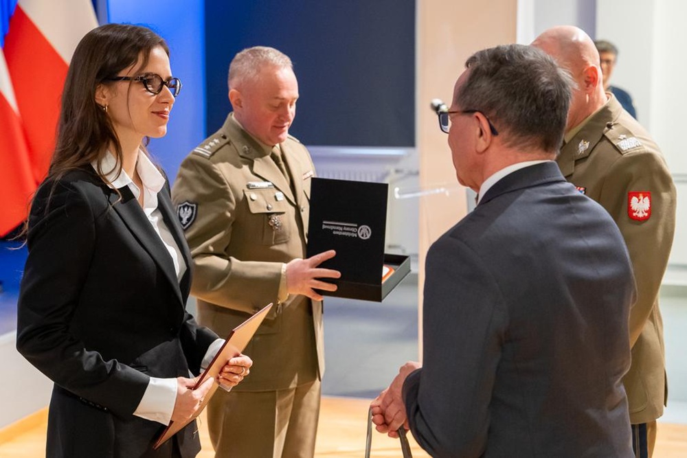 Dwóch oficerów i dwoje cywilów w trakcie wręczania nagrody.